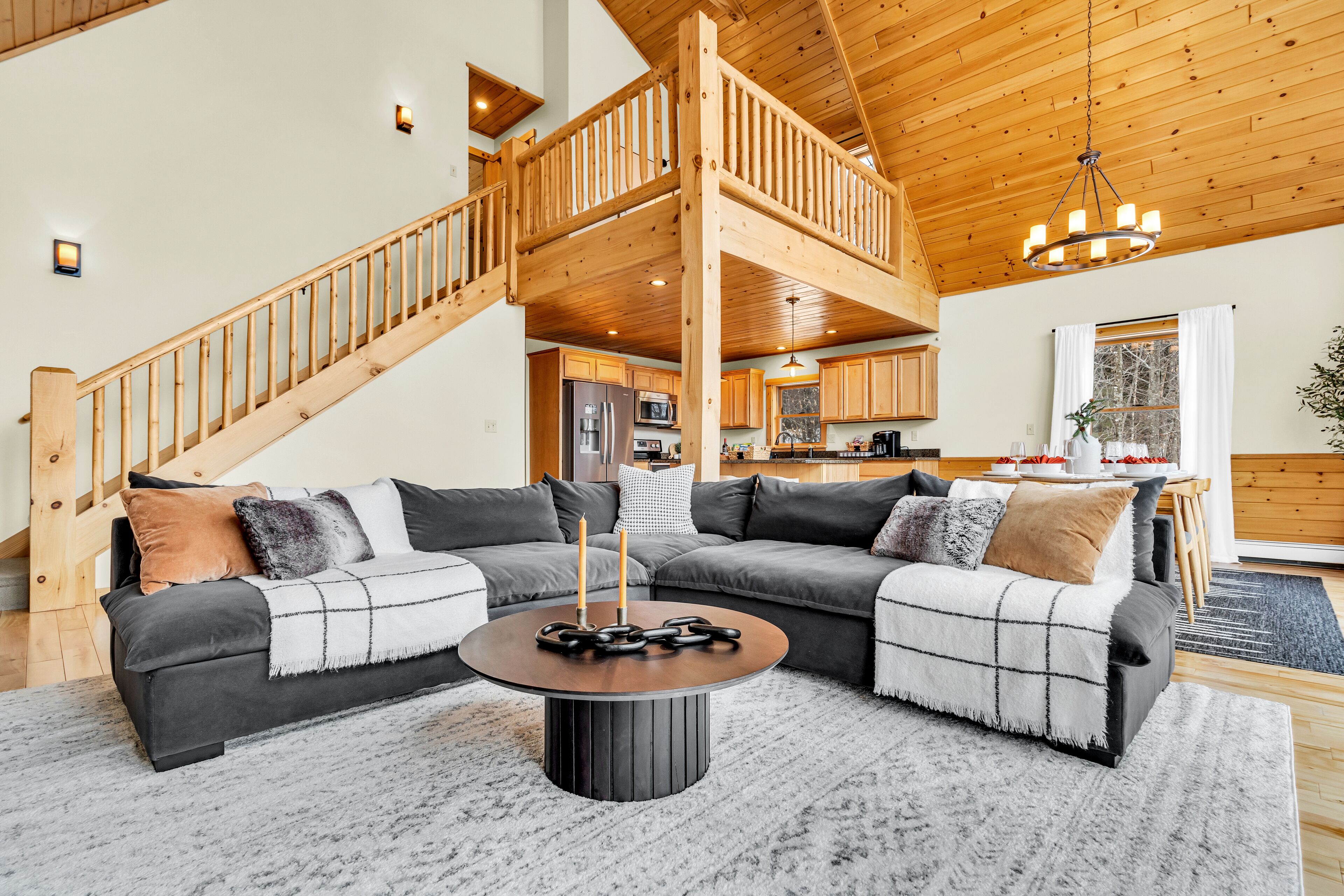 A spacious living room with a large sectional sofa, a round coffee table, and a wooden staircase leading to an upper level.