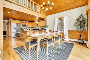 A spacious kitchen with wooden cabinets, a stainless steel refrigerator, and a dining area with a table set for four. - Sleeps 16+ Hot Tub with Mountain View - 3Min to Sunday River Ski - Game Room

 (Newry)