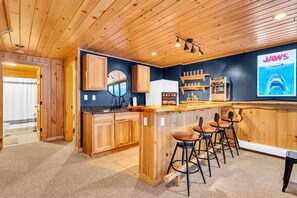A kitchen with wooden cabinets, a bar area with stools, and a poster of a shark on the wall. - Sleeps 16+ Hot Tub with Mountain View - 3Min to Sunday River Ski - Game Room

 (Newry)