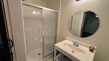 A bathroom with a shower, a sink, a mirror, and a towel rack.