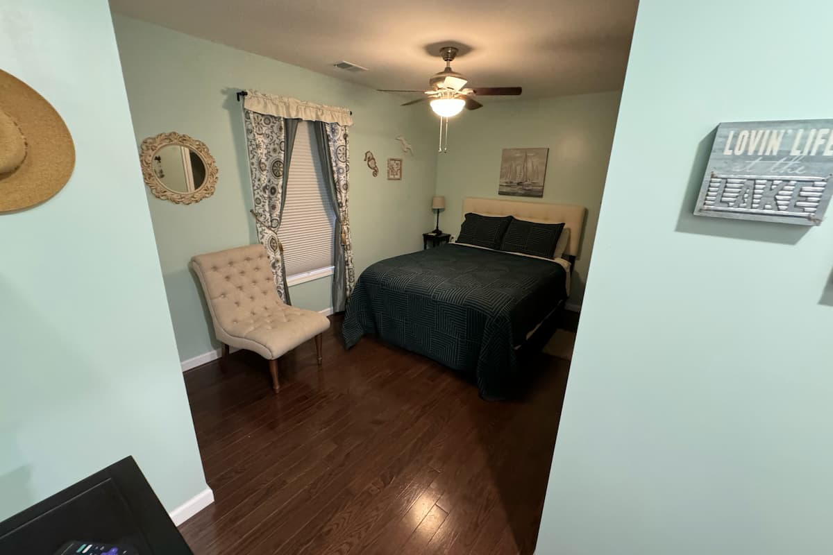 Une chambre à coucher comprenant un lit, une chaise, un ventilateur de plafond, un miroir et une œuvre d’art accrochée au mur.