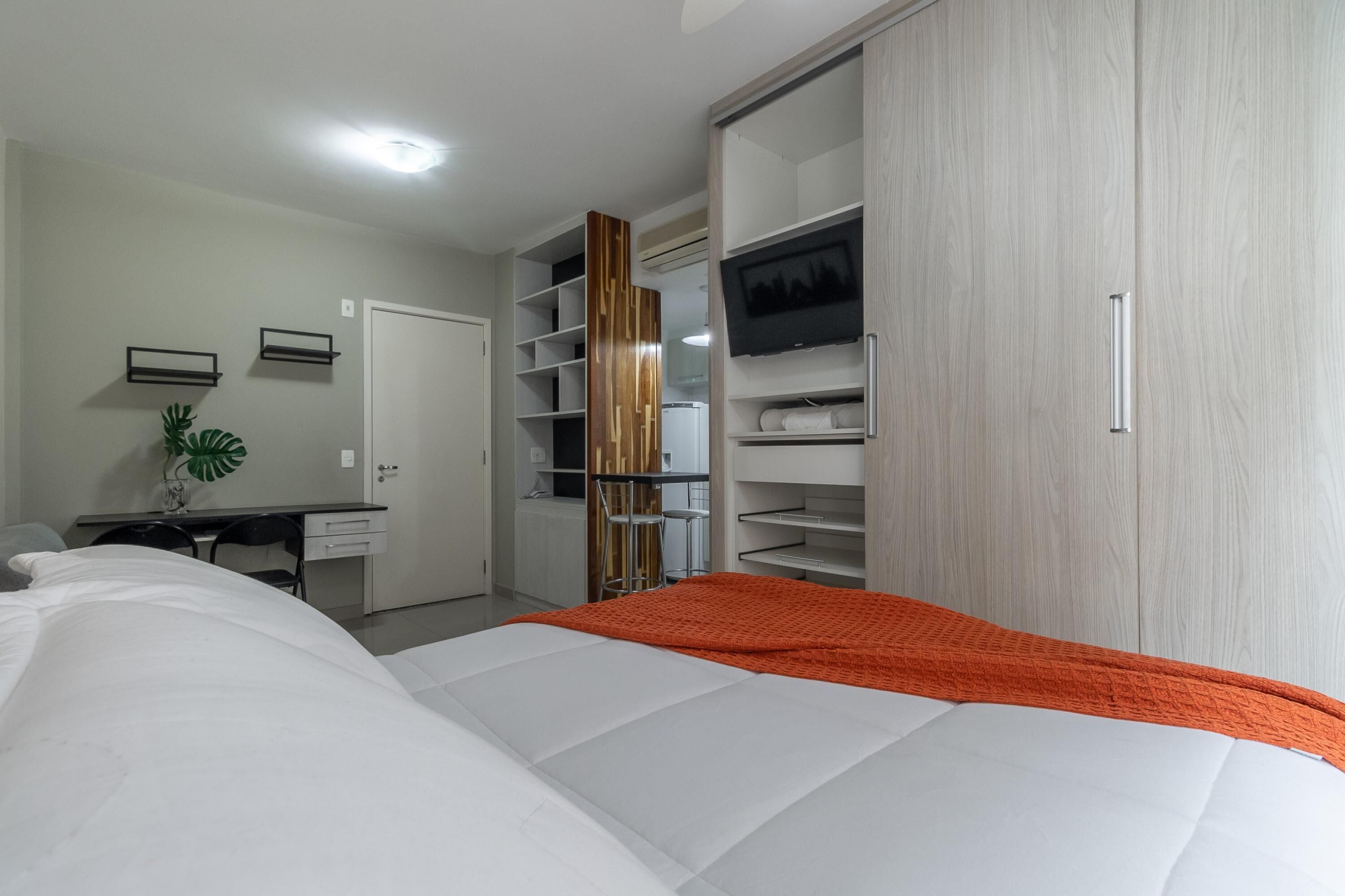 A bedroom with a bed, a desk, a chair, a wardrobe, and a TV.