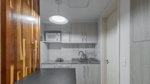A compact kitchen with a black countertop, white cabinets, a microwave, and a hanging rack. - Av0909 in S o Paulo (São Paulo)
