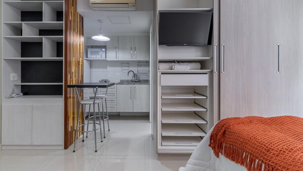A modern kitchen with white cabinets, a built-in microwave, and a dining area with bar stools. - Av0909 in S o Paulo (São Paulo)
