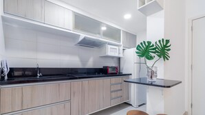 A modern kitchen with light wood cabinets, a black countertop, a microwave, and a red coffee machine. There are two wooden stools and a large green plant in a vase. - Av0905 in S o Paulo (São Paulo)