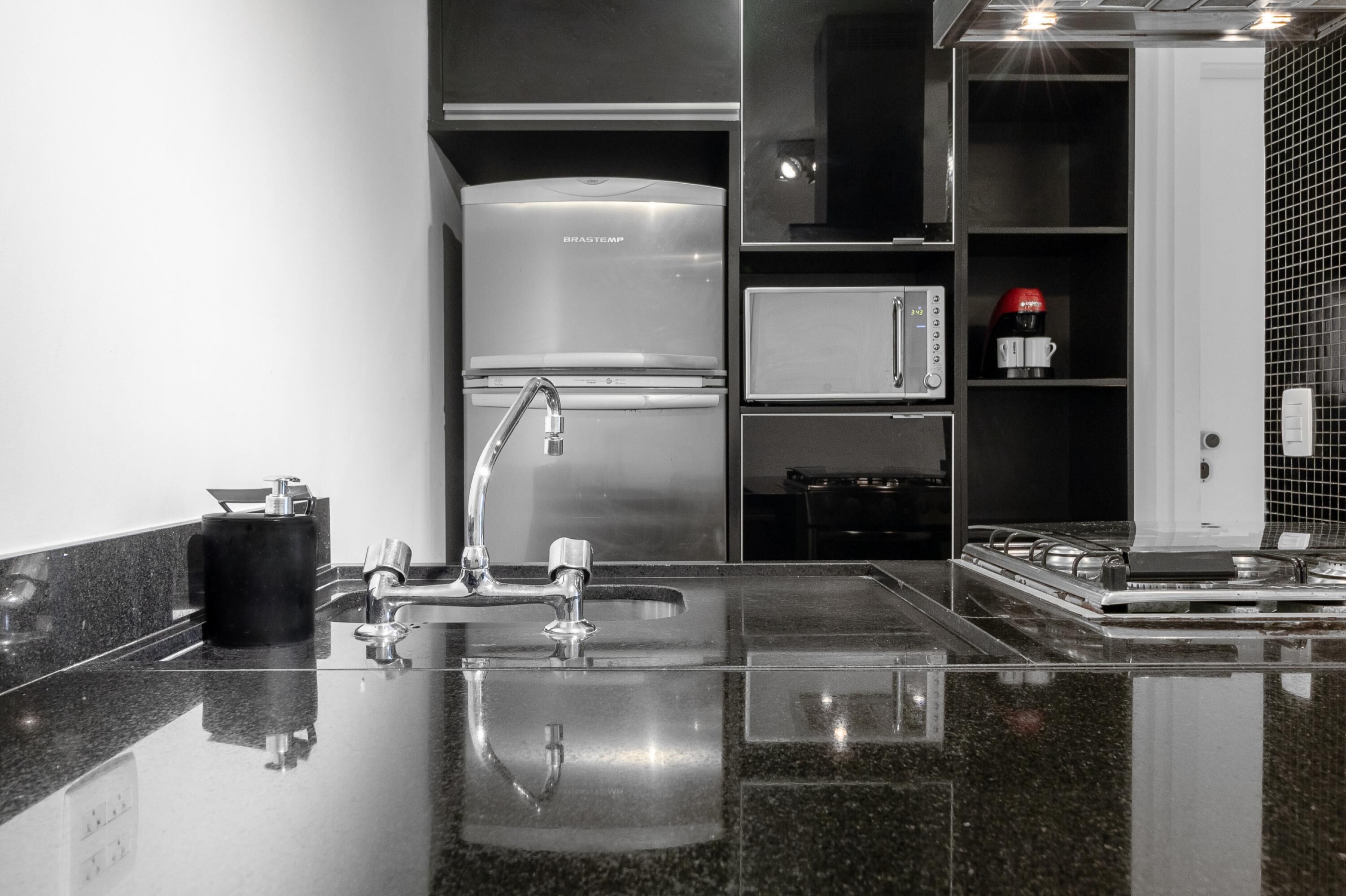 Uma cozinha moderna com frigorífico em aço inoxidável, máquina de café e pia com torneira.