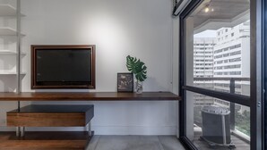 Ett modernt vardagsrum med ett konsolbord i trä, en väggmonterad TV och ett stort fönster med utsikt över stadsbilden.