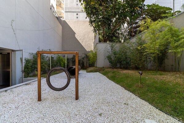 A courtyard with a tire swing, gravel ground, and a building in the background.