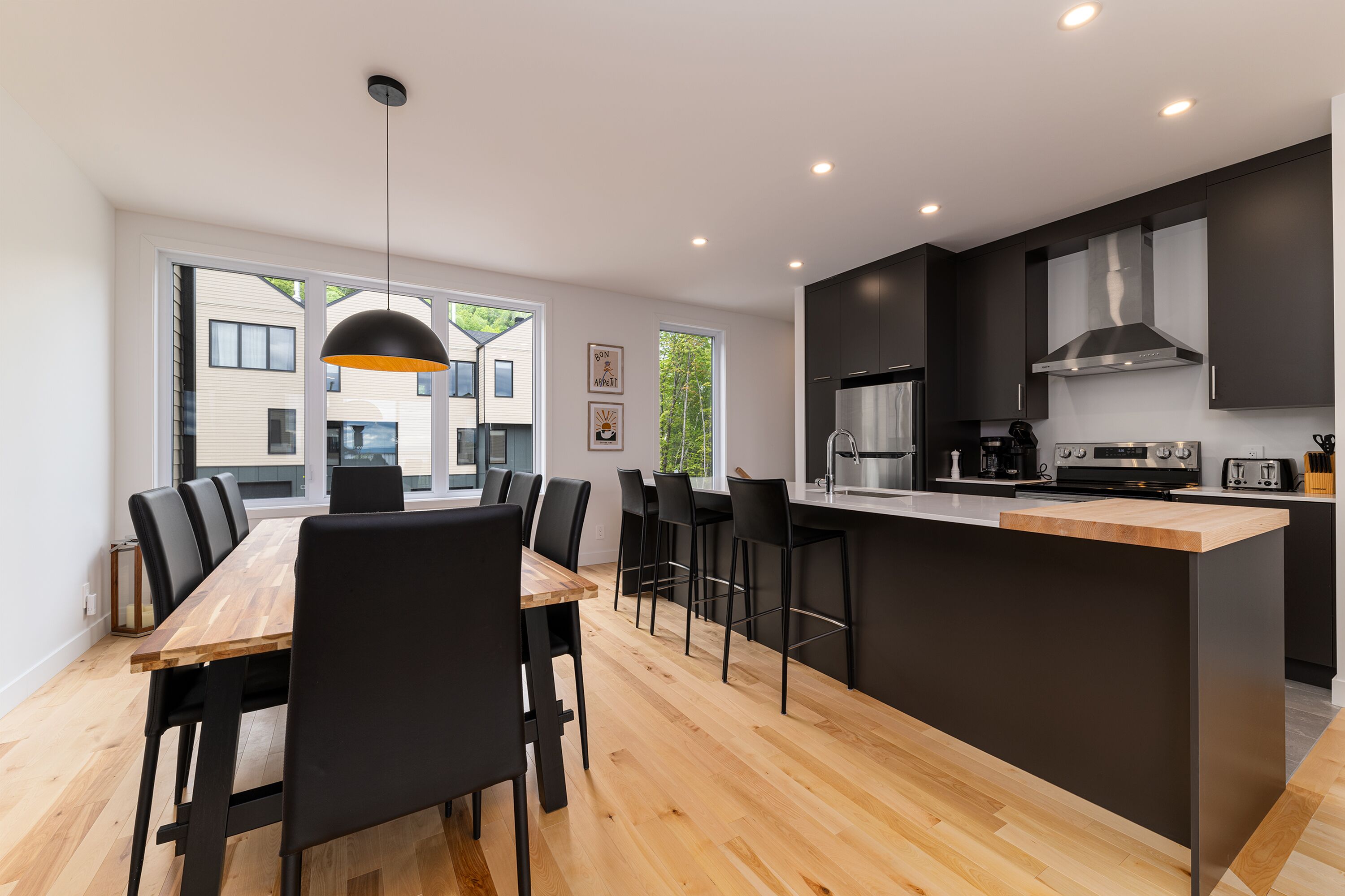 Una cocina moderna con una isla central, taburetes negros y un comedor con una mesa de madera larga y sillas negras.