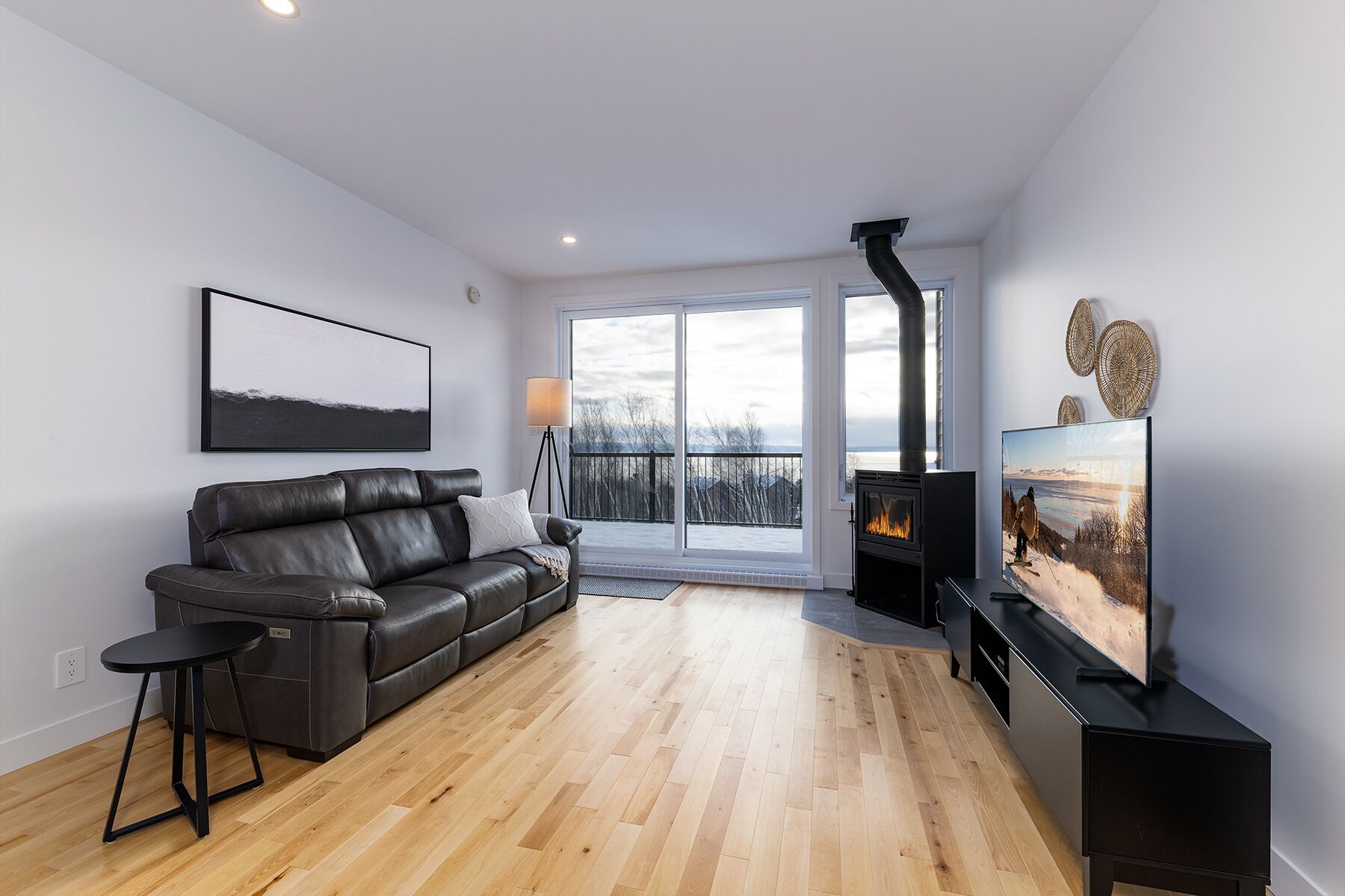 Una sala de estar moderna con un sofá de cuero, un televisor, una chimenea y un ventanal con vistas a un paisaje nevado.