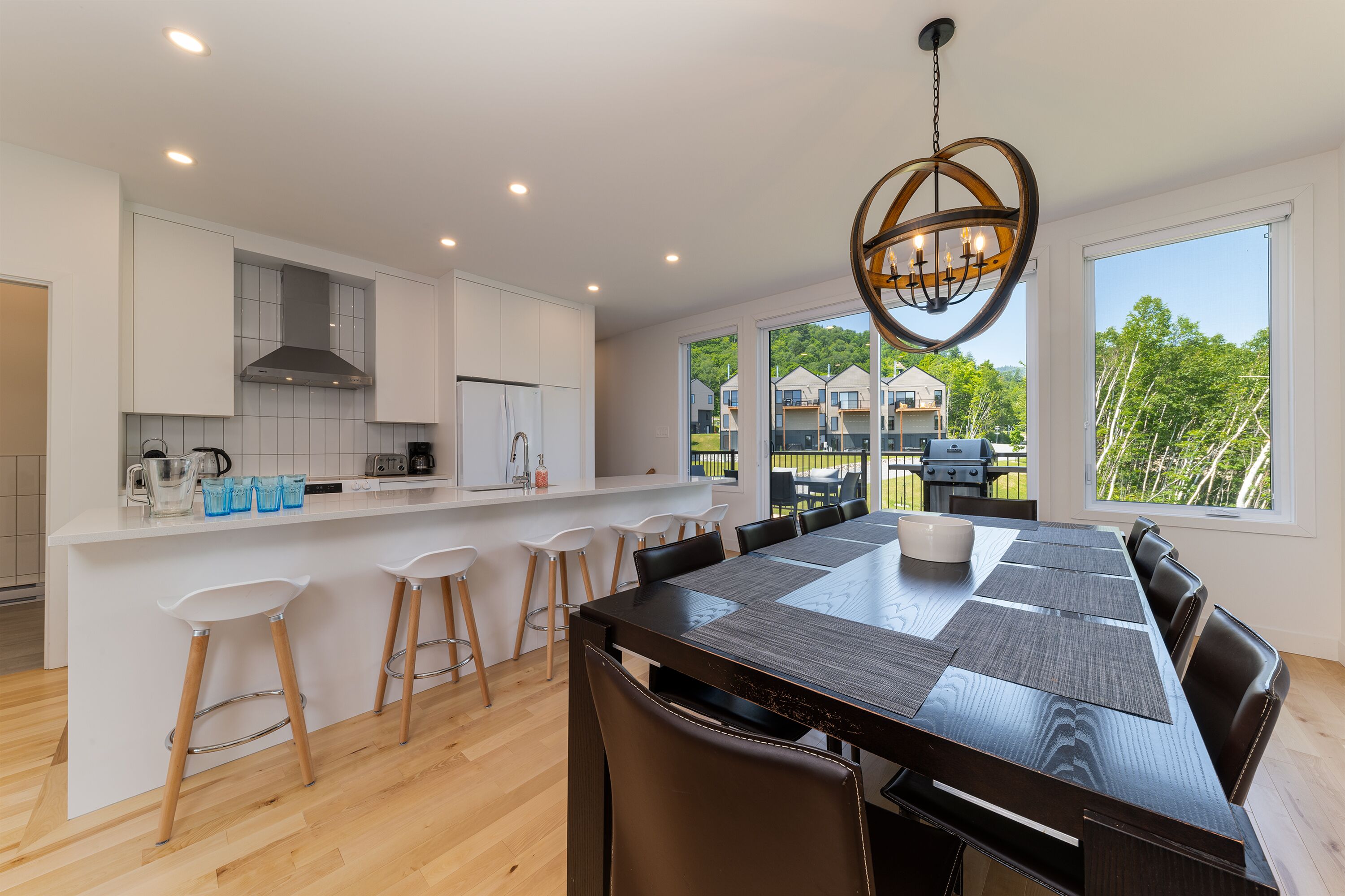 A modern kitchen with white cabinets, a large island with bar stools, and a dining area with a long table and chairs.