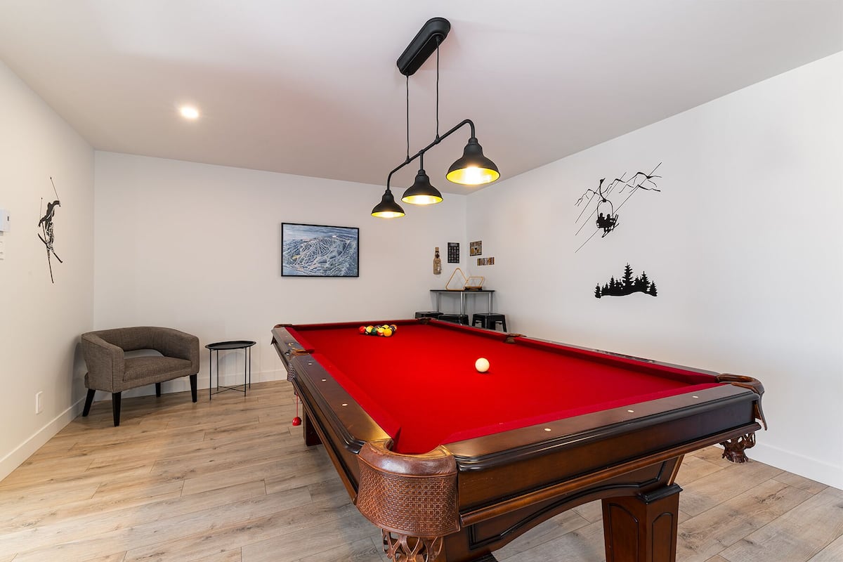 Une table de billard recouverte d’un drap de feutre rouge, un fauteuil gris et une petite table d’appoint.
