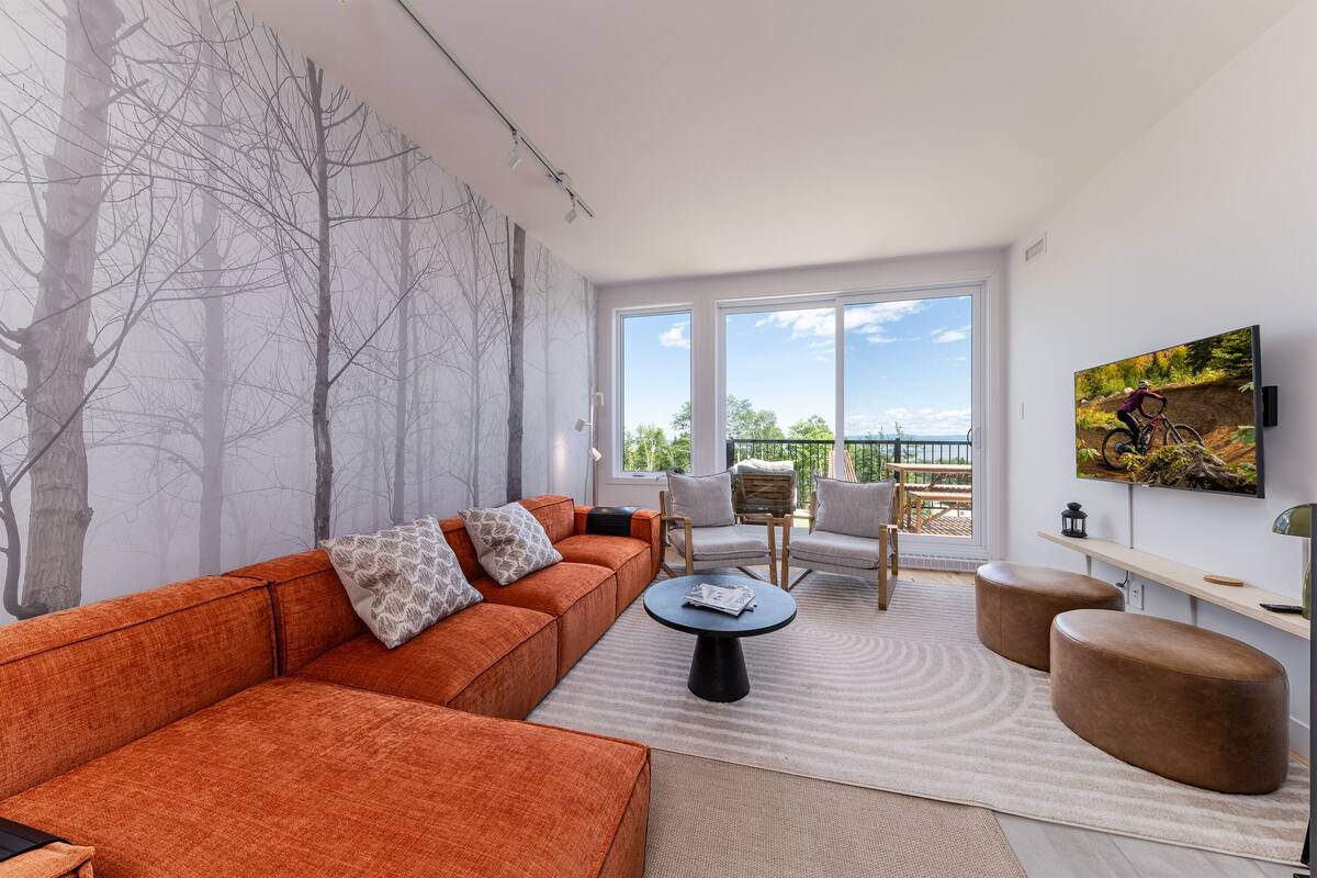 Un salon moderne avec un canapé d’angle, une table basse ronde et une vue sur l’extérieur grâce à de grandes fenêtres.