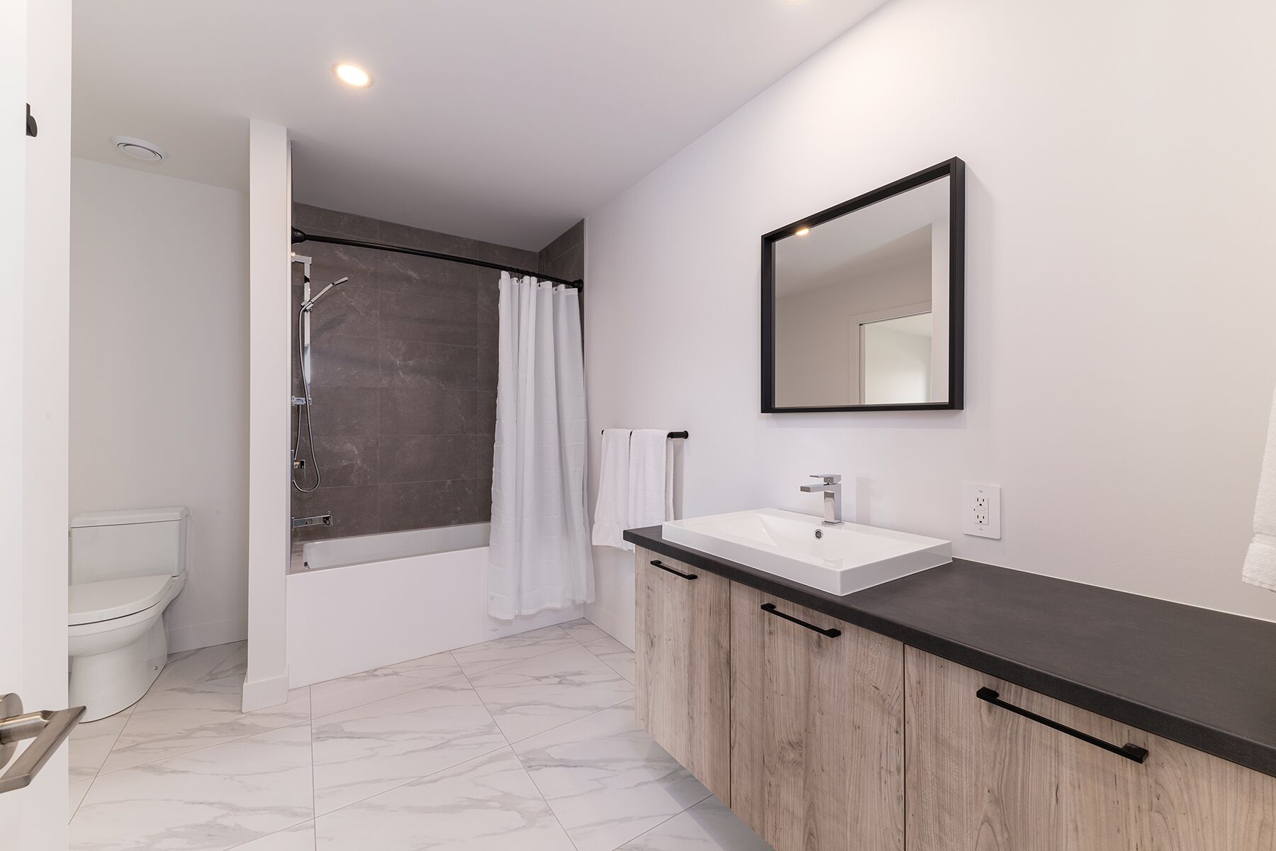 A modern bathroom with a white sink, wooden cabinets, a large mirror, and a shower area.