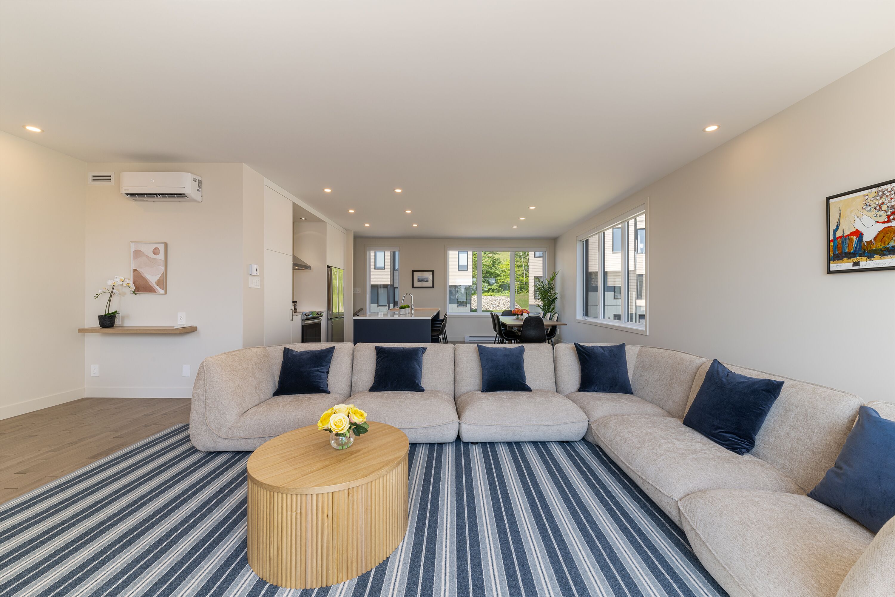 A modern living room with a beige sectional sofa, a round wooden coffee table, and a striped rug.