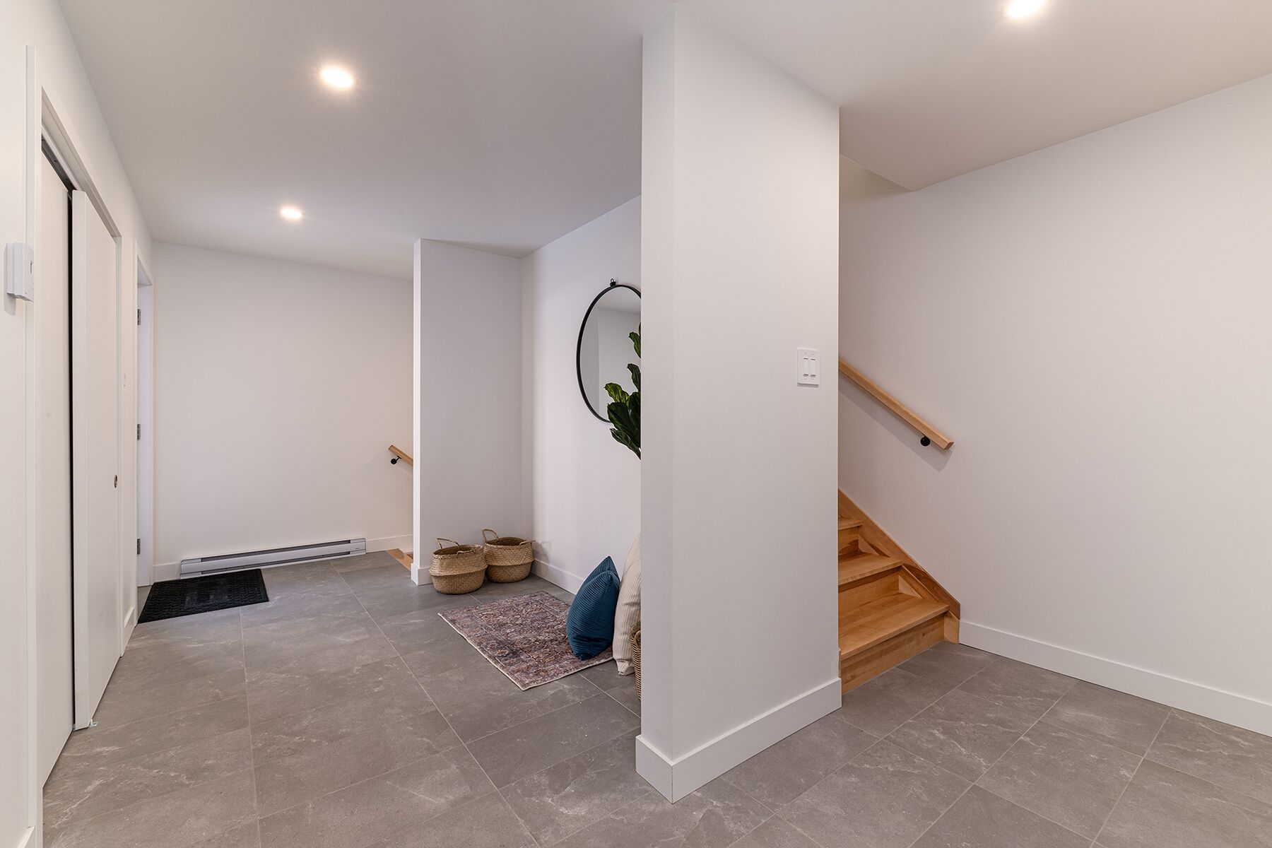 A modern hallway with a wooden staircase, a small rug, and a mirror on the wall.