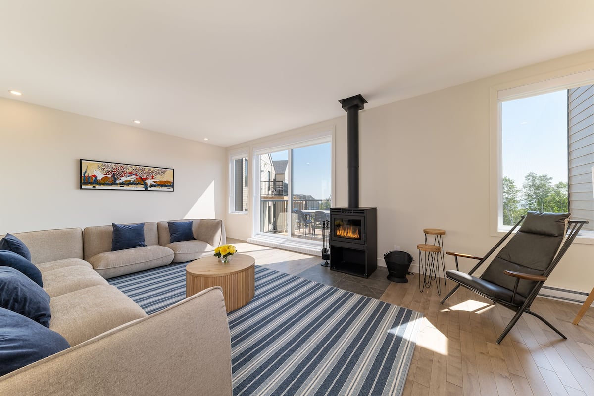 Un salon moderne avec un canapé, un tapis à rayures, une cheminée et une vue dégagée grâce à de grandes fenêtres.
