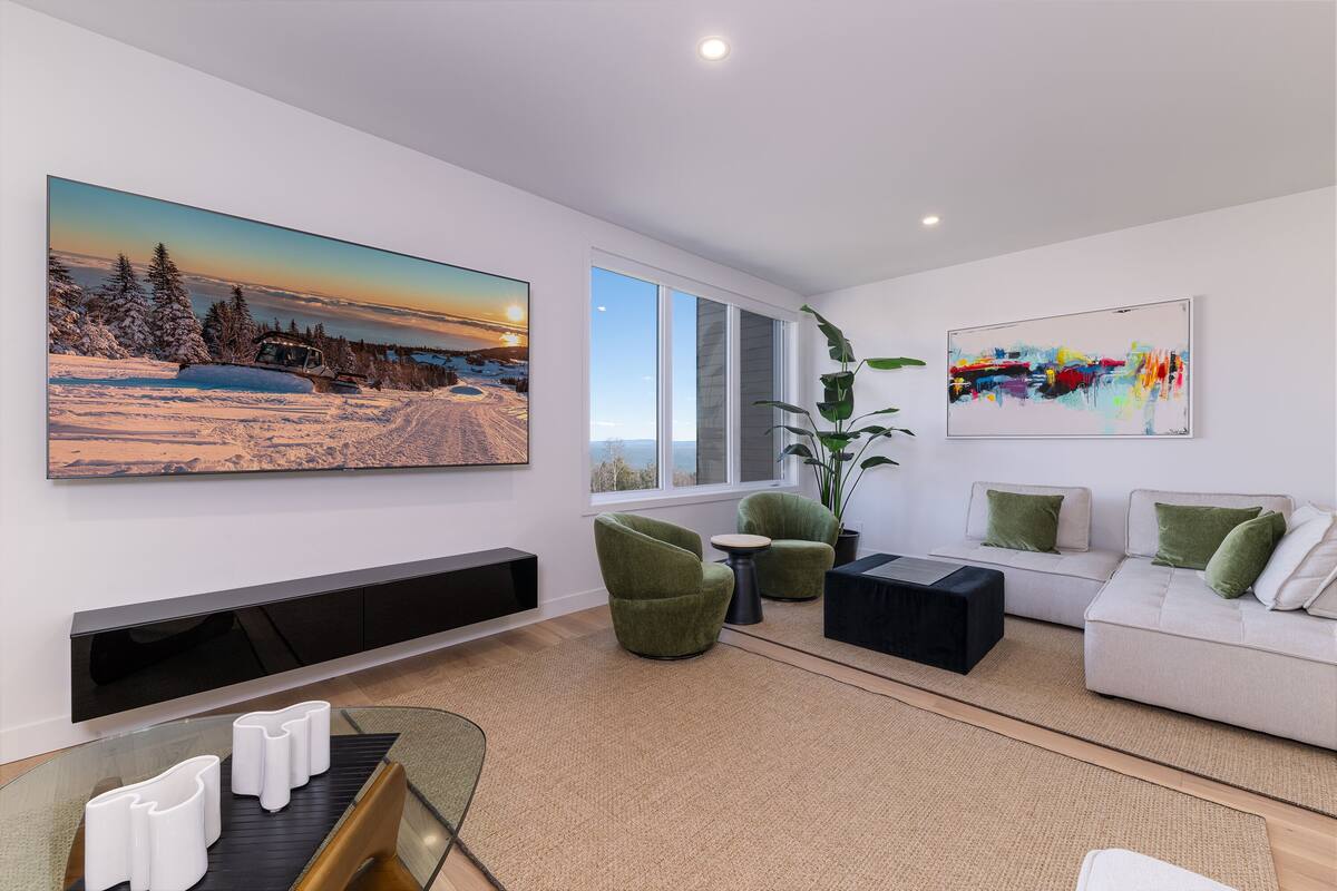 Un salon moderne avec un grand tableau représentant un paysage, un canapé, des fauteuils verts, une table basse et une plante.