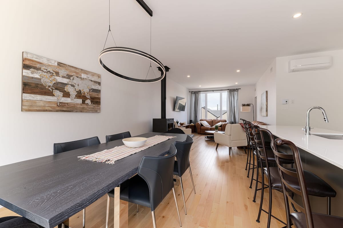 Une cuisine moderne avec une longue table à manger, des chaises noires et un luminaire suspendu.