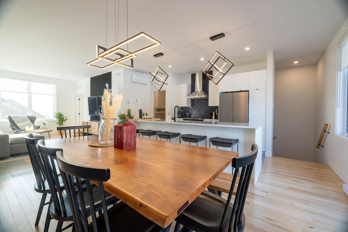 Une cuisine moderne avec une table à manger en bois, des chaises noires et des luminaires suspendus.
