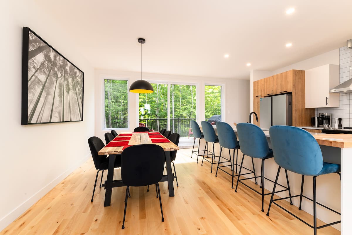Une cuisine moderne avec des meubles en bois, un réfrigérateur noir et un coin repas agrémenté d’une nappe rouge et de chaises noires.