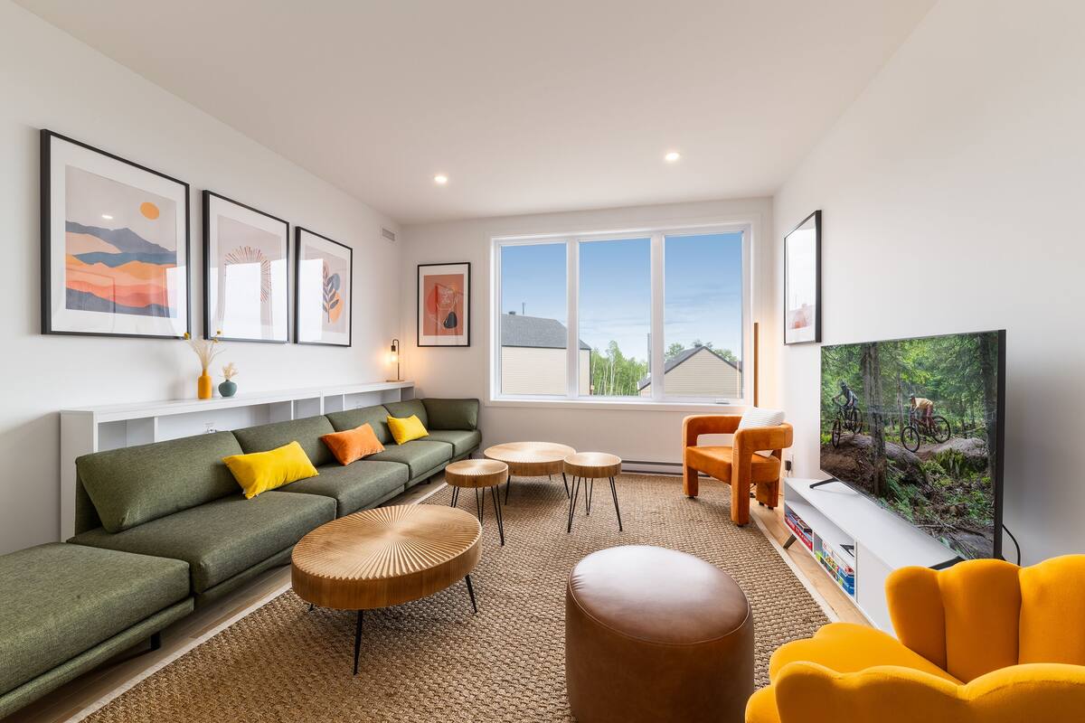 Un salon moderne avec un canapé vert, des fauteuils jaunes et un grand écran de télévision.