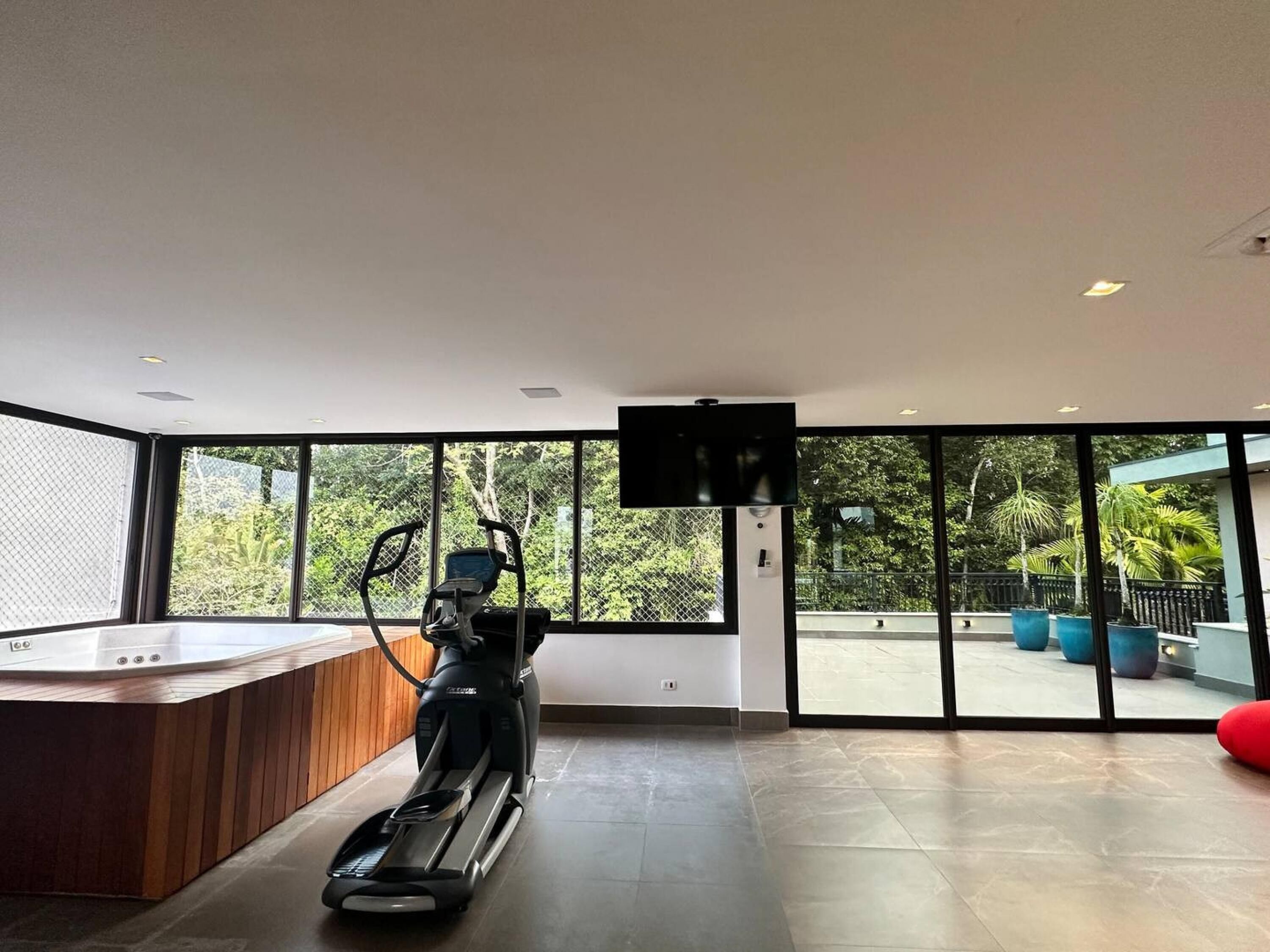 A modern room with a large window, a treadmill, a wooden counter, and a TV mounted on the wall.