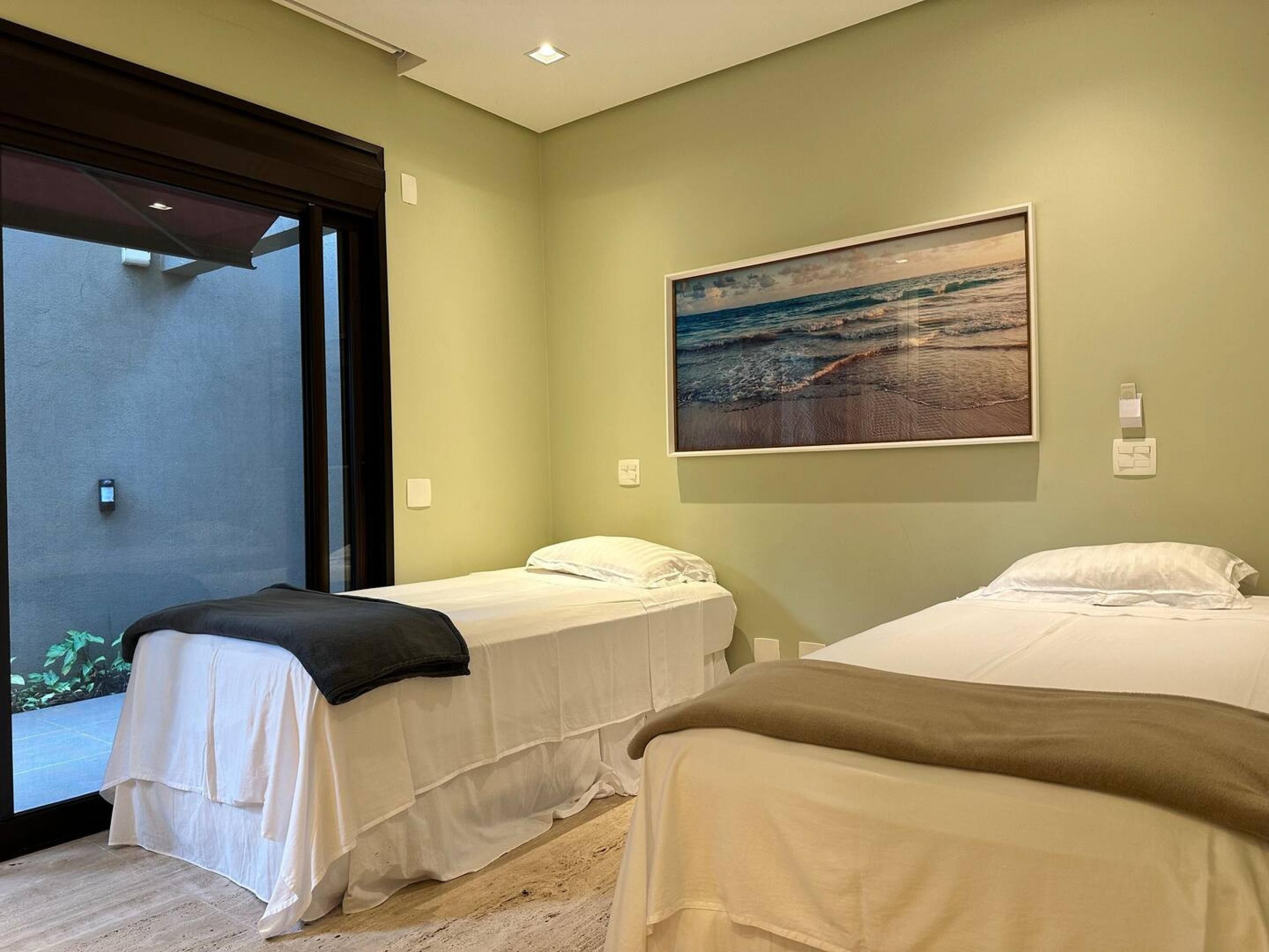 A hotel room with two beds, a large window, and a painting of a beach scene.