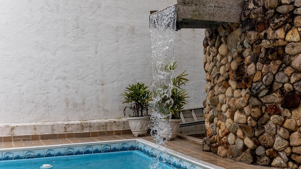 A swimming pool with a stone wall and potted plants. - Villagio Santa Mônica (Caraguatatuba)