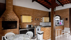 A kitchen with a brick wall, a microwave, a stove, and a TV. - Villagio Santa Mônica (Caraguatatuba)