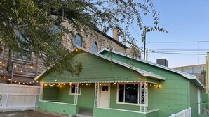 Un edificio verde con una recinzione bianca a picco, un portico decorato con luci e un piccolo giardino.