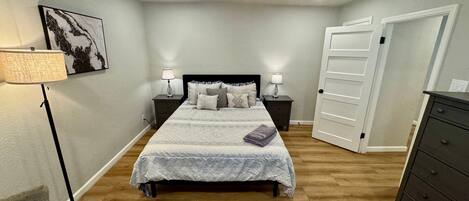 A bedroom with a bed, two bedside tables with lamps, a ceiling fan, a door, and a dresser.