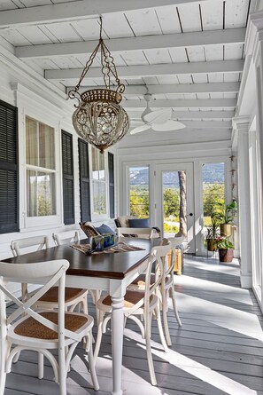 Une véranda abritée avec une table à manger et des chaises, un lustre et une vue sur l’extérieur.