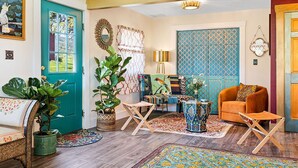 A cozy living room with a teal door, a large plant, a colorful sofa, and a patterned rug. -  Sparkle on the Rocks is a Sanctuary of Comfort and Artistic Inspiration (Wallingford)