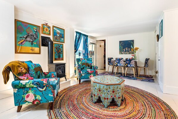 Una sala de estar con sofá, sillón y reposapiés, una chimenea y un comedor con sillas y una mesa.