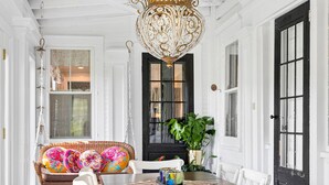 A dining area with a wooden table and white chairs, a hanging chandelier, and a black door with glass panels. -  Sparkle on the Rocks is a Sanctuary of Comfort and Artistic Inspiration (Wallingford)