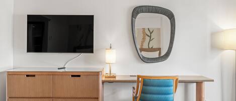 Moderni hotellihuone, jossa on puinen kaappi, työpöytä lampun kanssa, televisio, peili ja sininen tuoli.