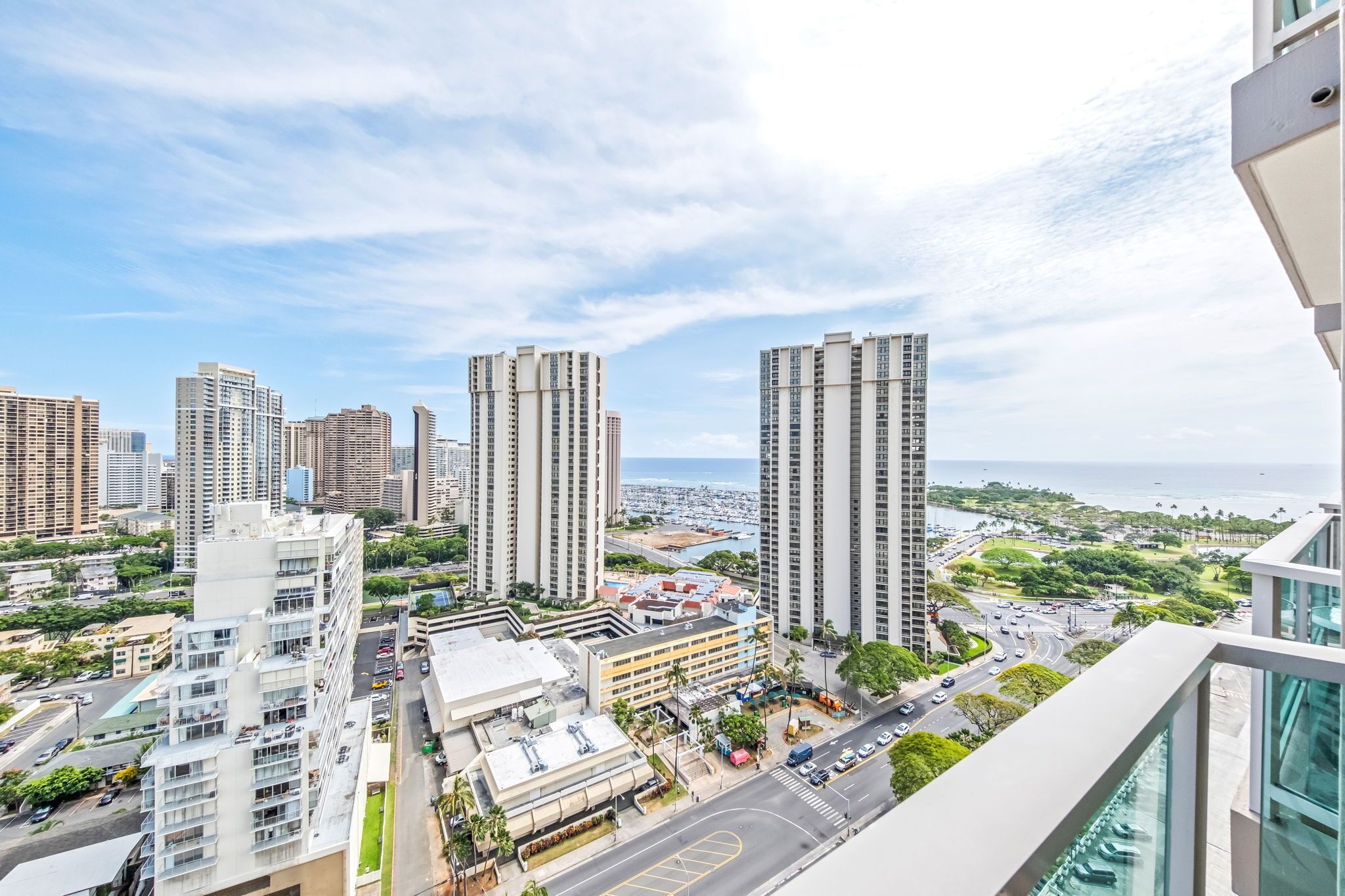 A high-rise building with multiple floors, a parking area, and a view of the cityscape and ocean.