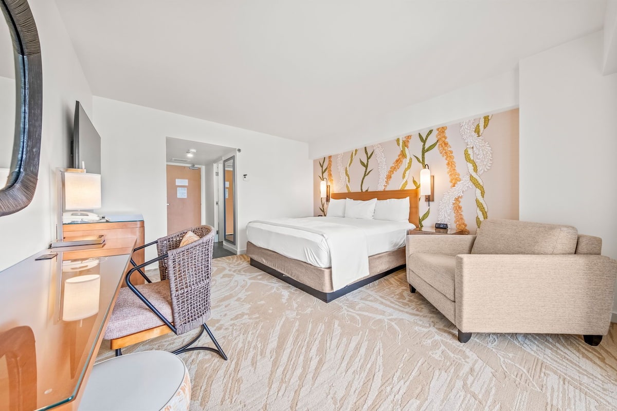 Ein Hotelzimmer mit einem Bett, einem Sofa, einem Schreibtisch mit Lampe und einem Sessel.