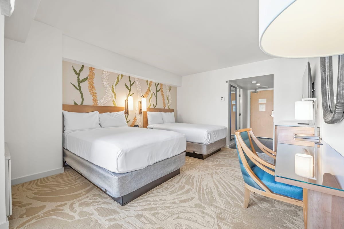 Ein Hotelzimmer mit zwei Betten, einem Schreibtisch mit Stuhl und einem großen Spiegel.
