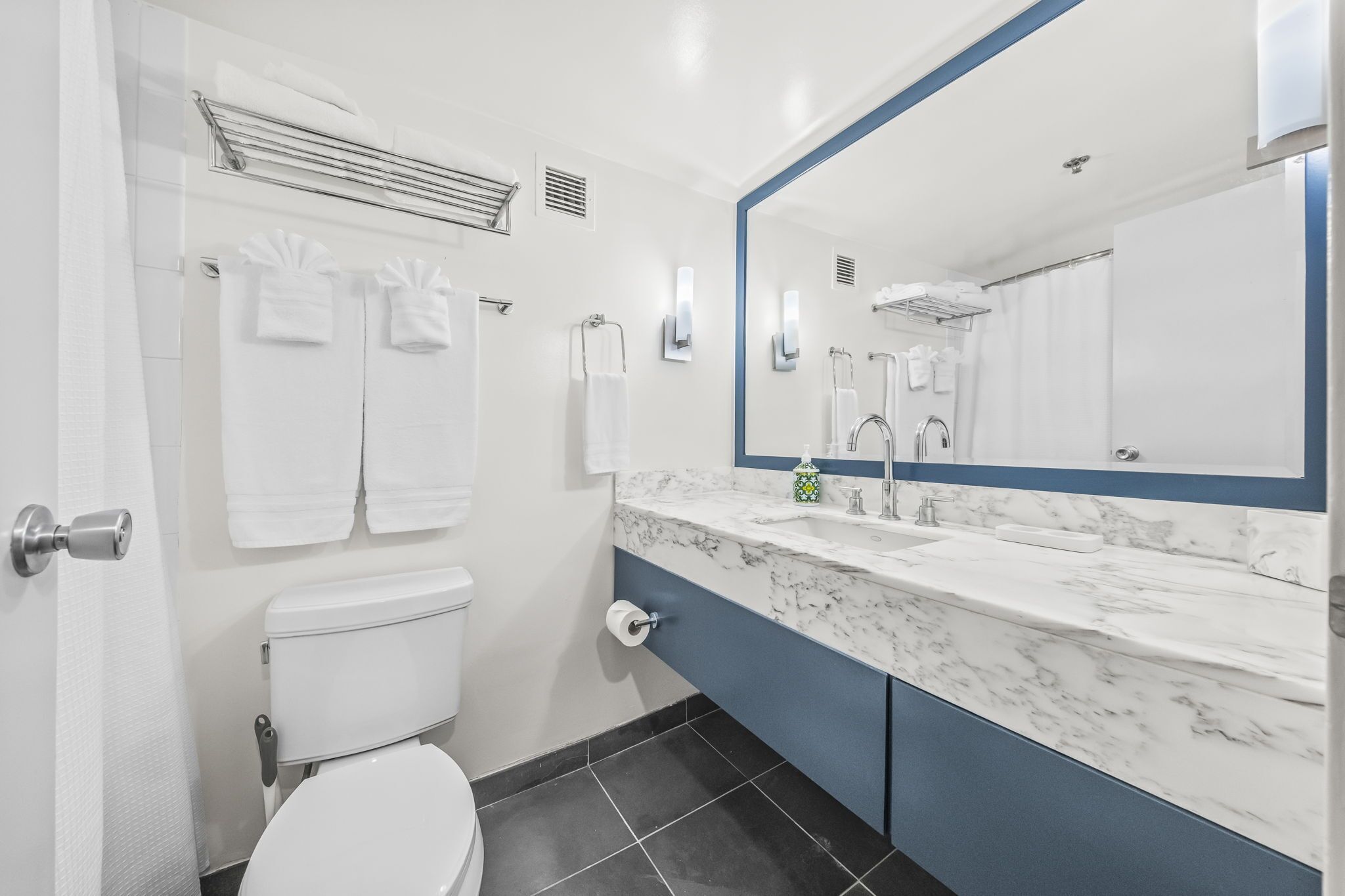 A modern bathroom with a white toilet, a marble sink, and a large mirror.