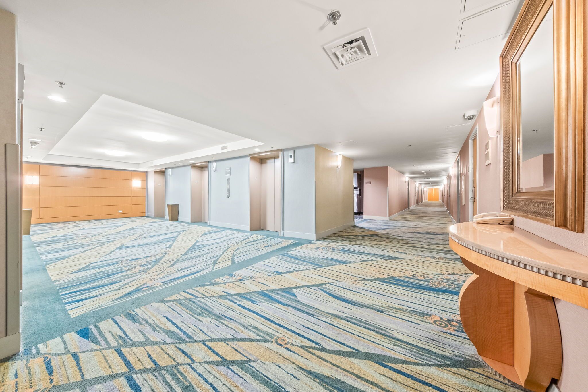 A hotel corridor with a patterned carpet, a wooden reception desk, and a large mirror.
