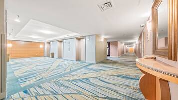 A hotel corridor with a patterned carpet, a wooden reception desk, and a large mirror.
