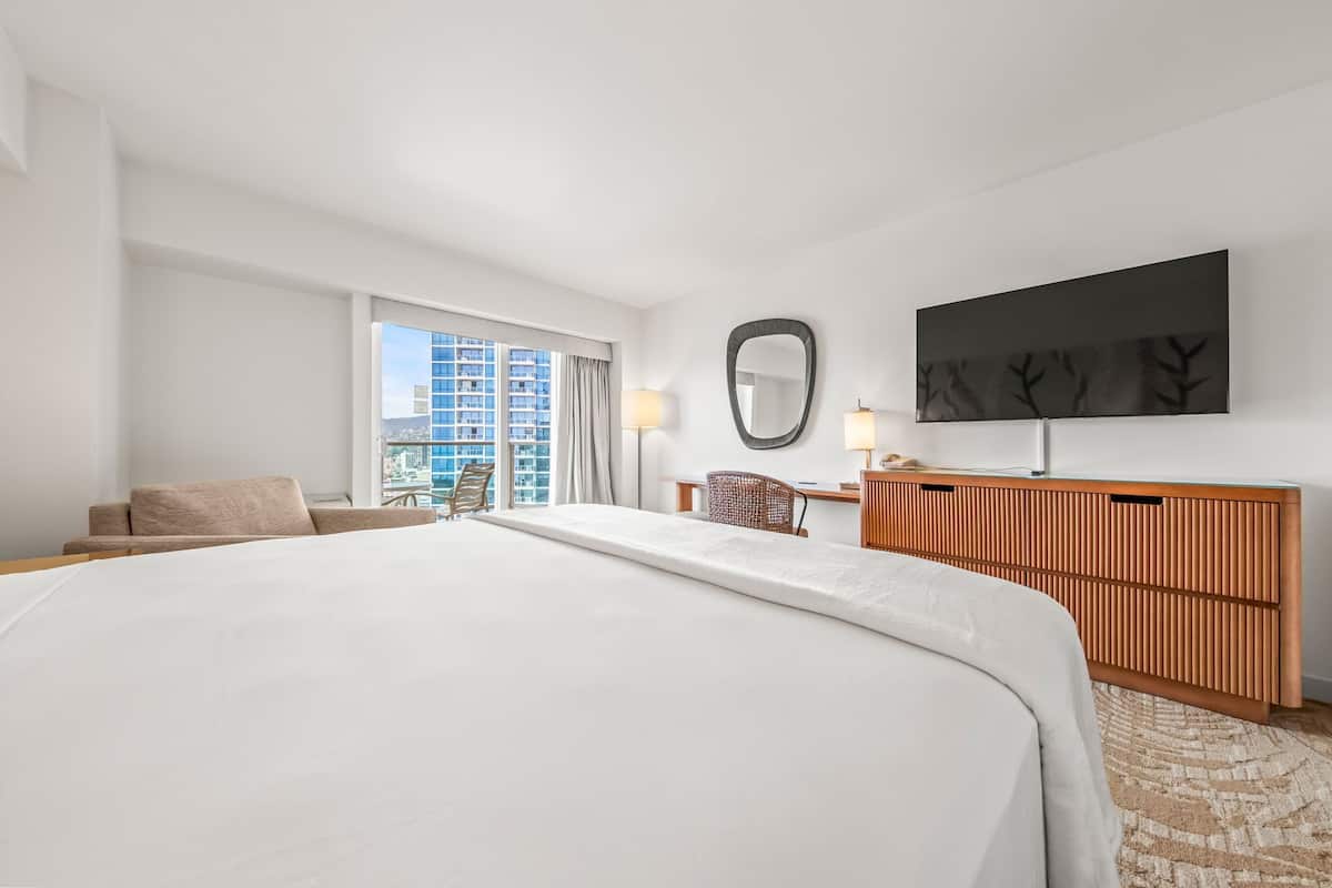 Ein Hotelzimmer mit einem großen Bett, einem Schreibtisch, einem Stuhl, einem Fernseher und einem Fenster mit Blick auf die Stadt.
