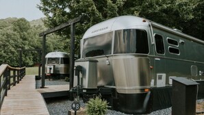 Ein Vintage-Airstream-Trailer vor einer hölzernen Anlegestelle mit einem kleinen Garten.