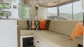 Ein gemütliches Wohnmobil-Interieur mit einer Sitzecke, einer kleinen Küchenzeile und Fenstern mit Blick auf Grünflächen.