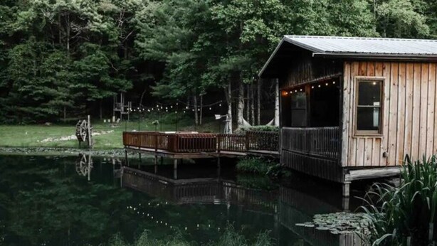 Une cabane en bois avec un quai s’avançant sur un lac paisible, le tout entouré d’une forêt dense.