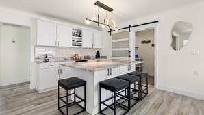 A modern kitchen with white cabinets, a marble countertop, and a central island with bar stools. - Waterfront! 1BR with private pool! 6 min. walk to the beach! (Treasure Island)