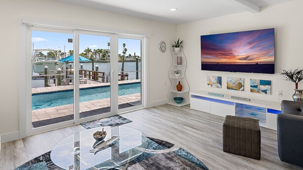 A modern living room with a glass table, a sofa, and a view of a pool area. - Waterfront! 1BR with private pool! 6 min. walk to the beach! (Treasure Island)
