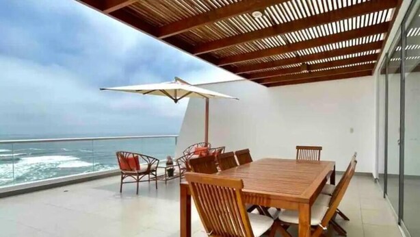 A wooden dining table with chairs and a large umbrella on a balcony with a view of the ocean. - Terrace with Jacuzzi, Duplex, Ocean View, Grill (Punta Hermosa)